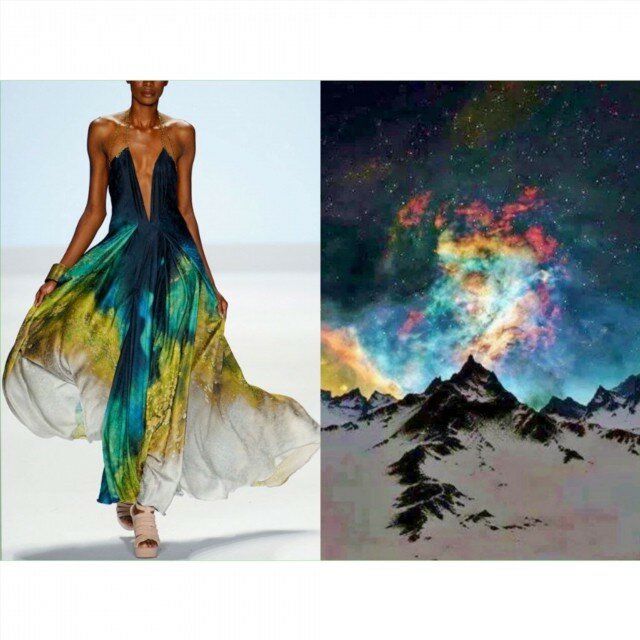 the image shows a woman in a beautiful gown standing on a runway. the gown is green, blue, and white and has a swirling, abstract design. the background is a snowy mountain range against a night sky with the aurora borealis, which is similar to the pattern on the dress.