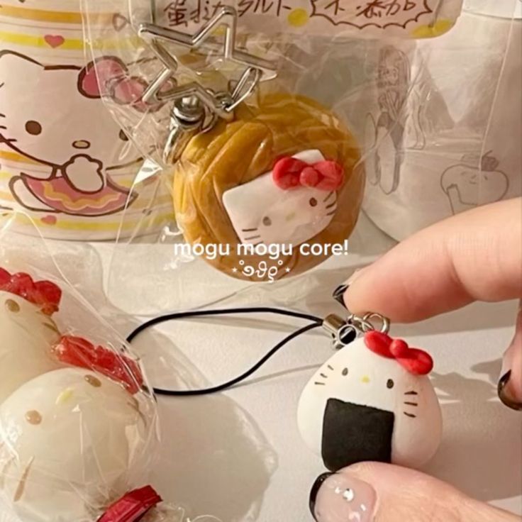 the image shows a collection of hello kitty themed keychains and accessories. the items are foodshaped, including an onigiri (rice ball) and egg tart, decorated with hello kitty's face and bow. there is a hello kitty cup in the background as well.