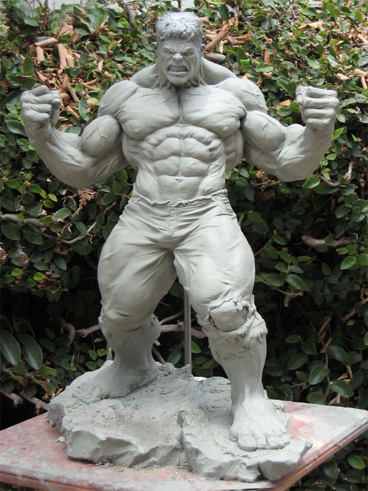 a clay sculpture of the hulk, a popular marvel comics superhero, stands in an aggressive pose against a backdrop of green foliage. the sculpture captures the hulk's immense muscularity and enraged expression. the natural lighting highlights the details of the clay work.