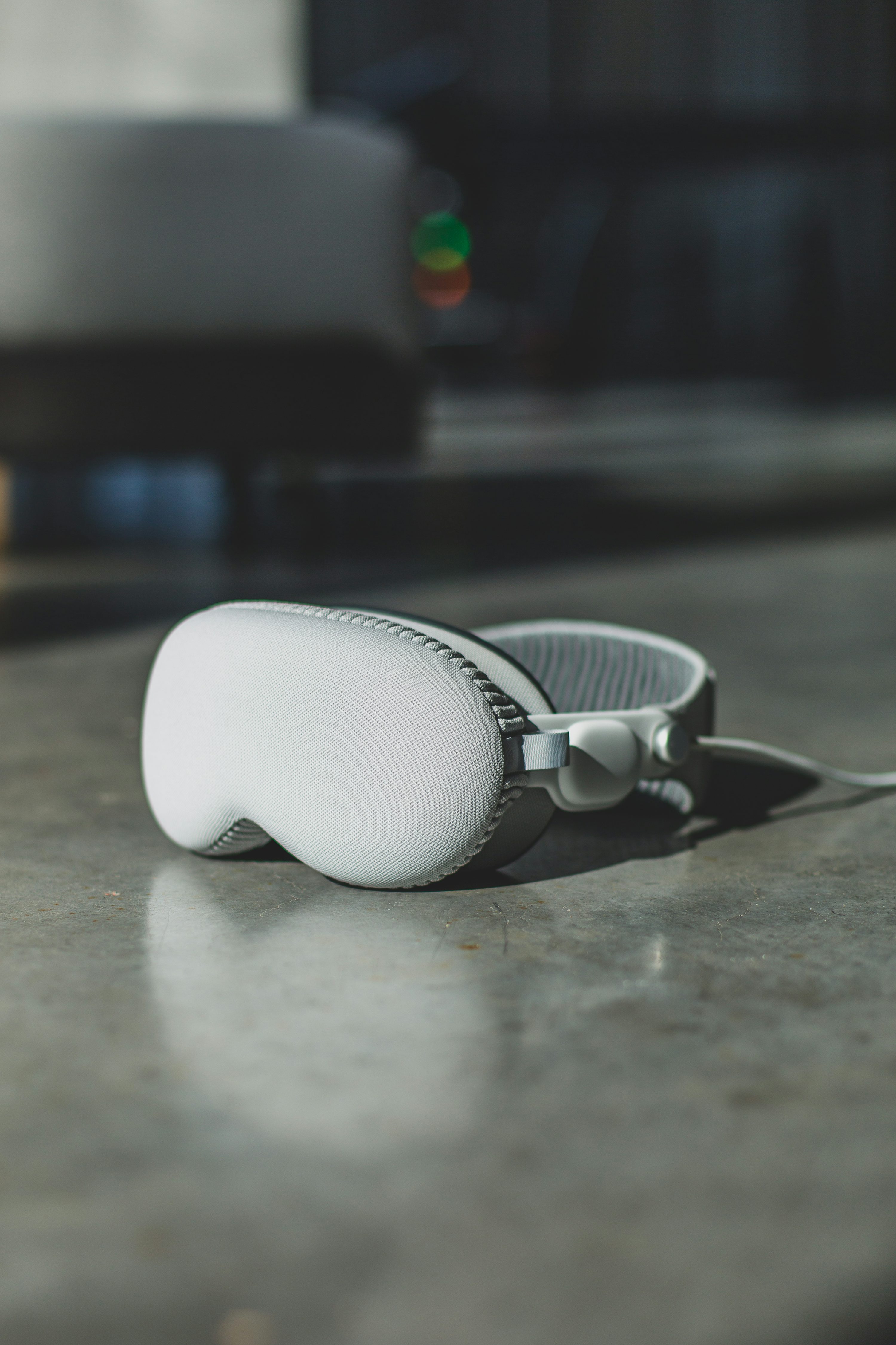 a pair of white headphones lying on a gray concrete table, with a car in the background. the headphones are the main focus of the image, and the background is blurred. the lighting creates shadows on the table and the headphones.