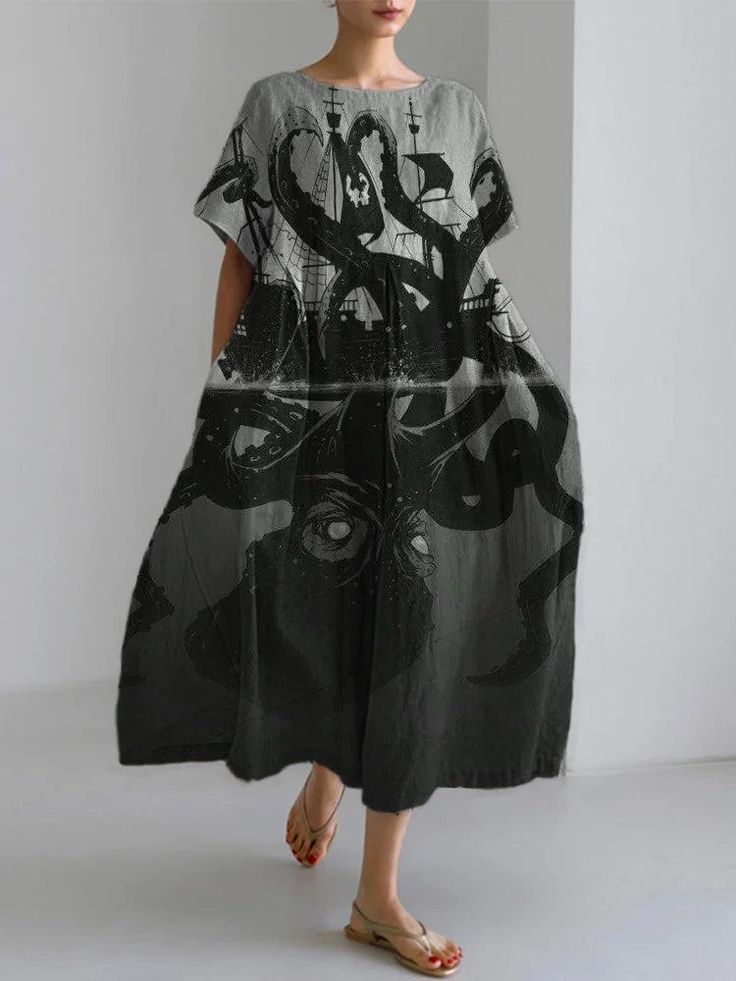 a woman is wearing a sleeveless, gray, loosefitting dress with an octopus and a ship print on it. the dress is a casual summer dress with a maxi length. the woman is wearing a pair of gold sandals.  she is looking at the camera with a slight smile. the background is a plain white wall.