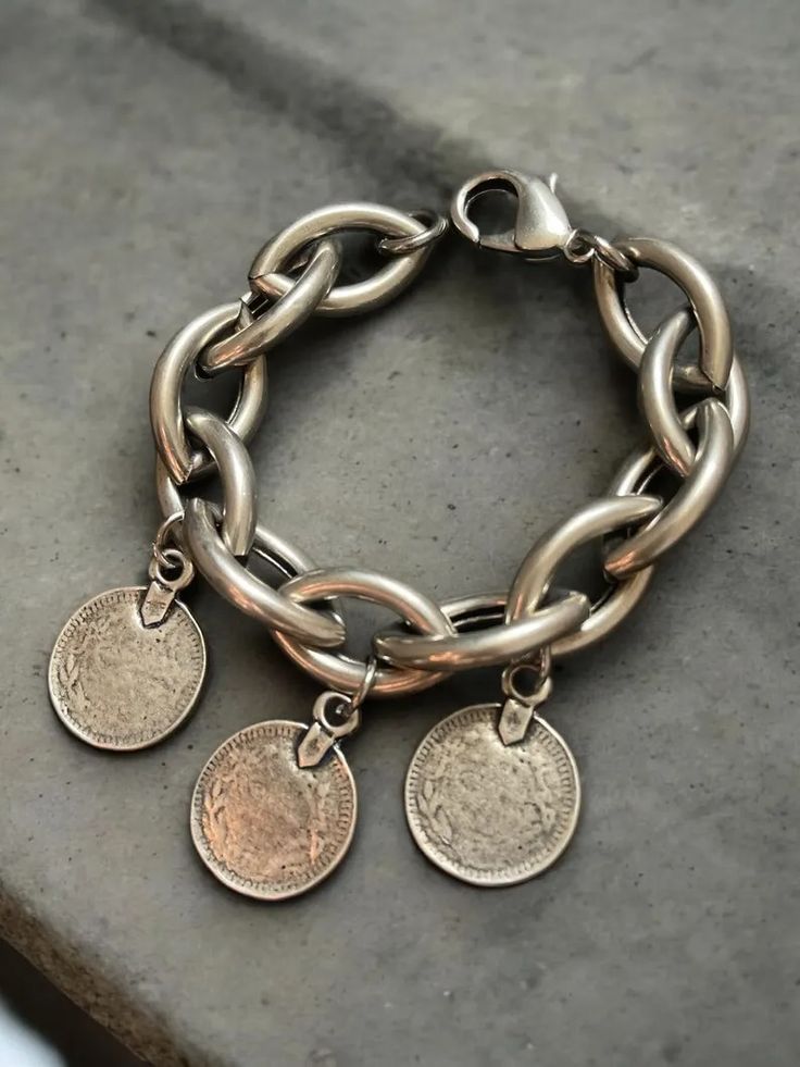 a closeup shot of a silver bracelet with chain links and decorative coin charms. the bracelet has an antique look and feel, with a boho chic style.