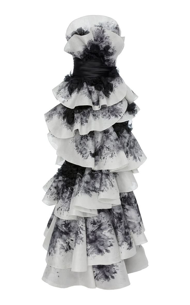 a white strapless dress with ruffles and a black floral design is featured in a studio shot. the dress has multiple tiers of fabric. a black ribbon is tied around the upper part of the dress, creating a cinched waist. the dress is adorned with ruffles and a black floral design.
