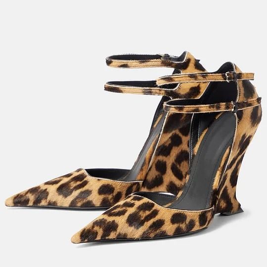 a pair of women's leopard print high heel shoes are shown.  the shoes have a pointed toe, a wedge heel, and ankle straps. the leopard print is a light brown and dark brown calf hair. the shoes appear to be made of highquality materials and have a stylish and elegant design.