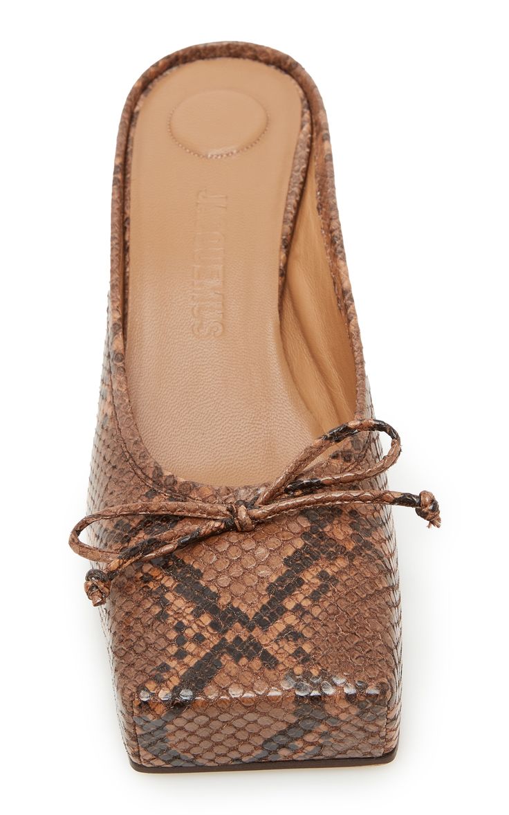 a closeup, studio shot of a pair of women's aeyde mules.  the shoes are made of brown snakeskin leather, have a square toe, and feature a small bow detail at the vamp.  the inside of the shoe shows a light brown leather insole. the background is white.