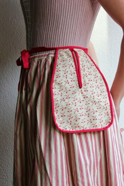 a person is wearing a striped skirt and a floral apron with a red ribbon tie. the skirt has red and white stripes, and the apron has a floral pattern with a red border. the person is wearing a top, but it is not fully visible. the style of the outfit appears to be vintageinspired.