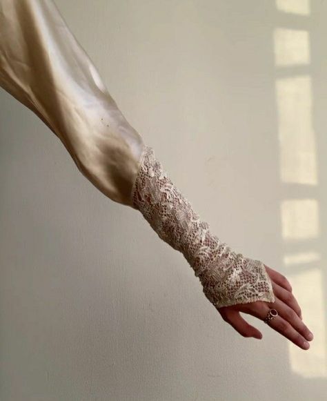 an arm and hand wearing a dress sleeve adorned with lace, highlighted by natural light.