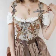 a woman models a vintage, floral corset and skirt with lace accents on her top.  she wears a delicate necklace with a pendant. the image is a closeup shot of her from the chest up.