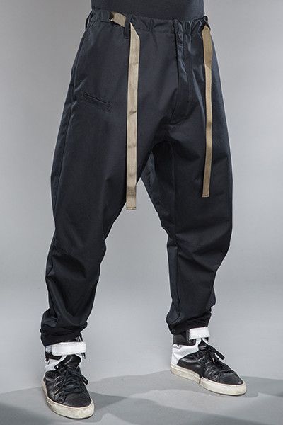 a man is standing wearing a pair of black drawstring jogger pants. the pants have a relaxed fit and are gathered at the ankles. he is also wearing a pair of white sneakers. the background is a light gray.