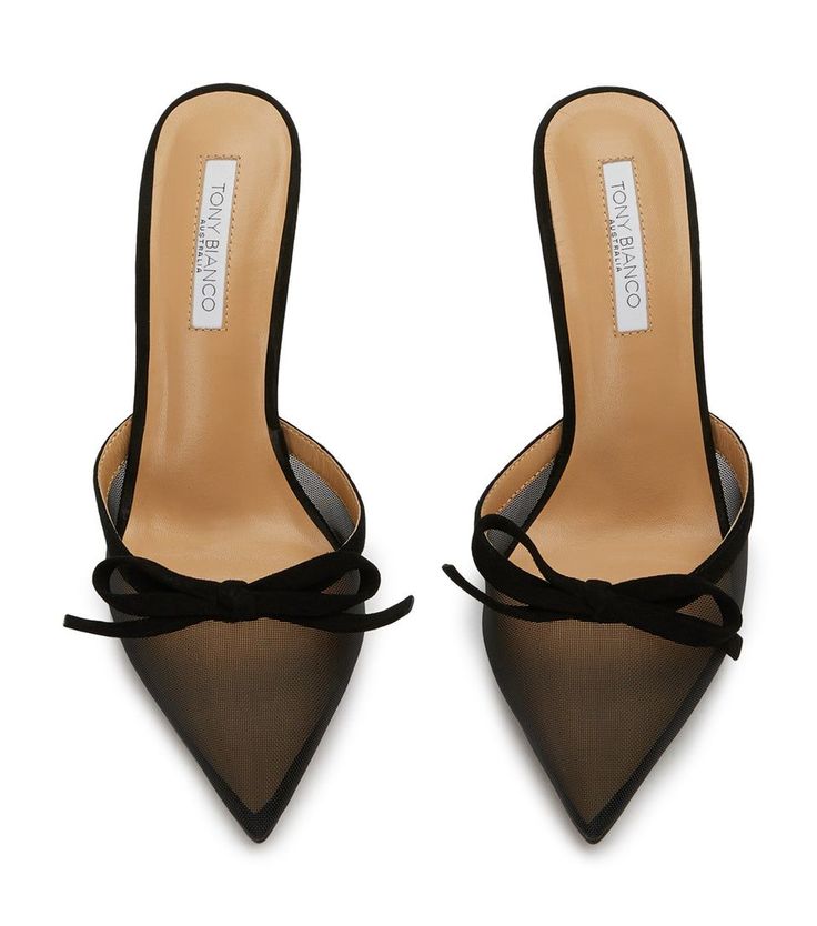 a pair of black tony bianco women's heeled mules are displayed against a white background. the shoes are pointedtoe and feature a mesh upper with a suede bow detail.  the insole is visible, showing the tony bianco branding. the shoes are positioned with a slight angle, showcasing both the front and side profile.