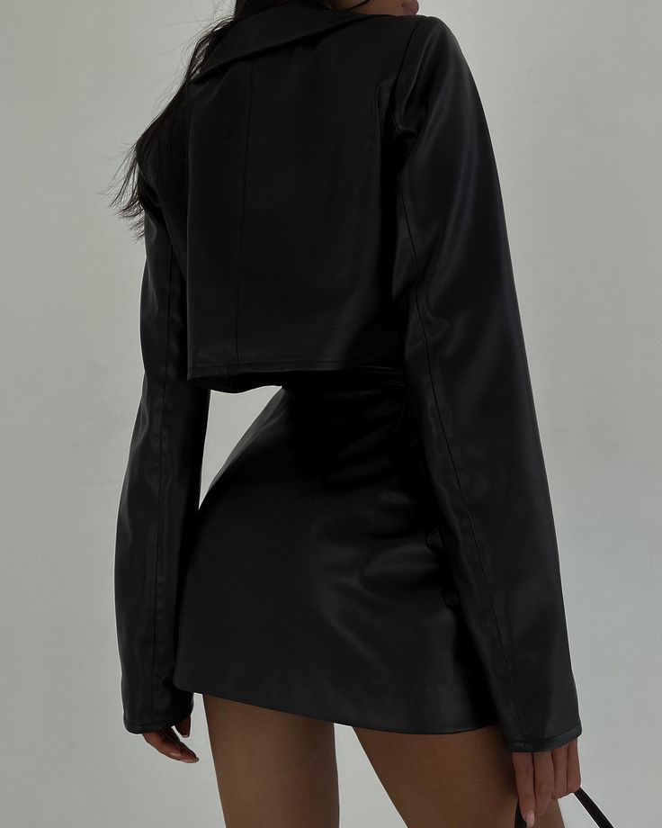 a woman is seen from the backside, wearing a black leather jacket and skirt. the jacket is short, ending just above the waist. the skirt is a mini skirt.