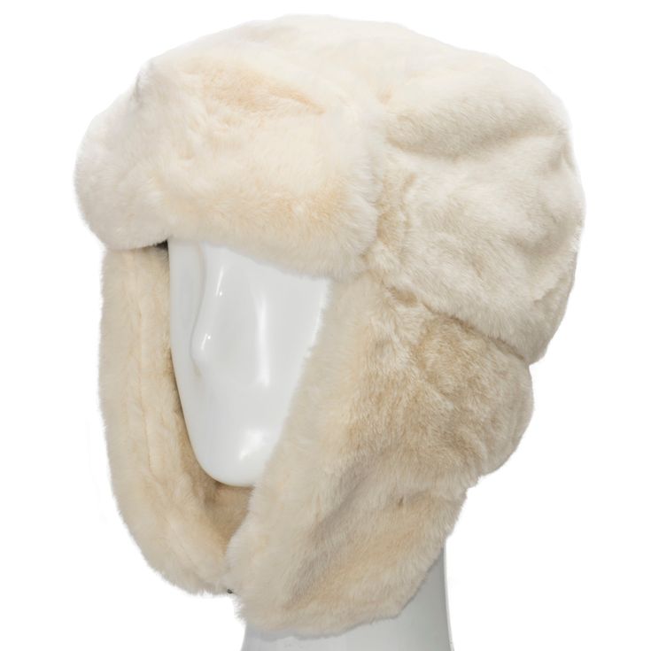 a white faux fur hat with ear flaps is displayed on a white mannequin. the hat is made of soft, fluffy fur and appears to be very warm. it is a stylish and practical accessory for winter.