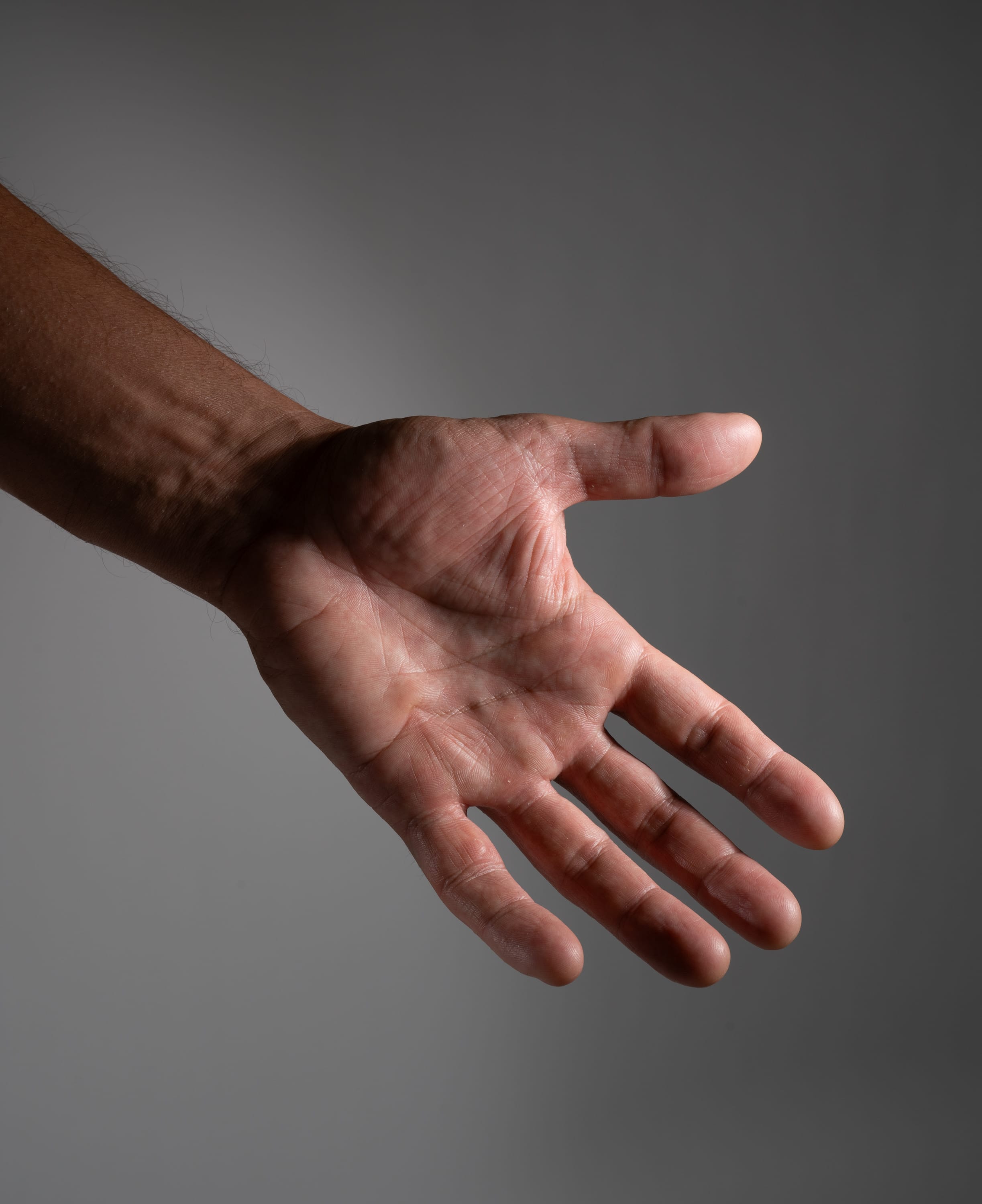 the image showcases a closeup of a man's hand extended palm up against a neutral gray background. the hand is illuminated dramatically, highlighting the texture and details of the skin.