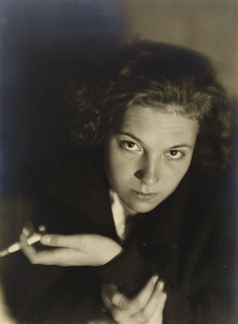 a captivating black and white portrait of a young woman from the 1920s or 1930s.  she is shown from the chest up, with dark, curly hair framing her face. her expression is serious and intense, and she holds a cigarette between her fingers. the background is dark and shadowy, drawing focus to the woman and her expressive eyes. the overall style is moody and elegant, reminiscent of art deco photography. the image conveys a sense of mystery and sophistication.