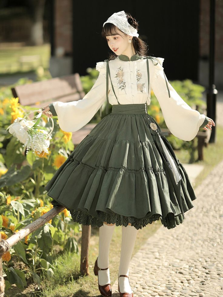 a young woman in a vintageinspired outfit poses in a garden. she's wearing a white embroidered top with long, flowing sleeves, paired with a long green skirt. the skirt is full and falls in soft pleats, creating a romantic silhouette. her outfit is complemented by a delicate headband and white stockings. she holds a small bouquet of flowers and smiles gently towards the camera. the soft lighting and natural surroundings enhance the dreamy and romantic atmosphere of the photograph.