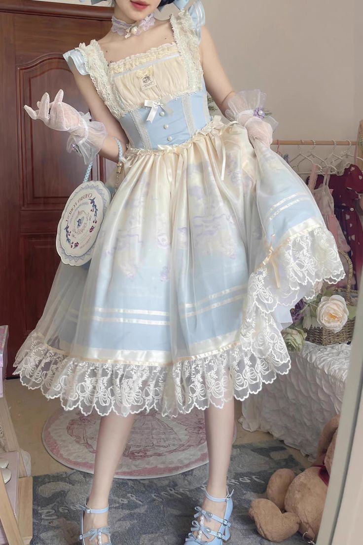 a young woman is posing in a bedroom, wearing a light blue and cream lolita dress. she is holding a blue and white purse and her outfit is accessorized with bows and lace. the photo appears to be a mirror selfie.