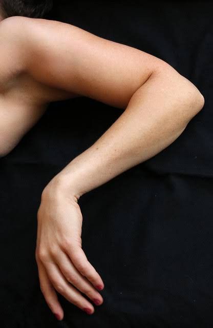 a woman's arm is outstretched and relaxed.  the fingers are extended and slightly curled.  the skin is smooth and the nails are painted a dark red.  the arm is resting on a black surface. the woman is laying prone, and her arm is bent at the elbow and wrist.