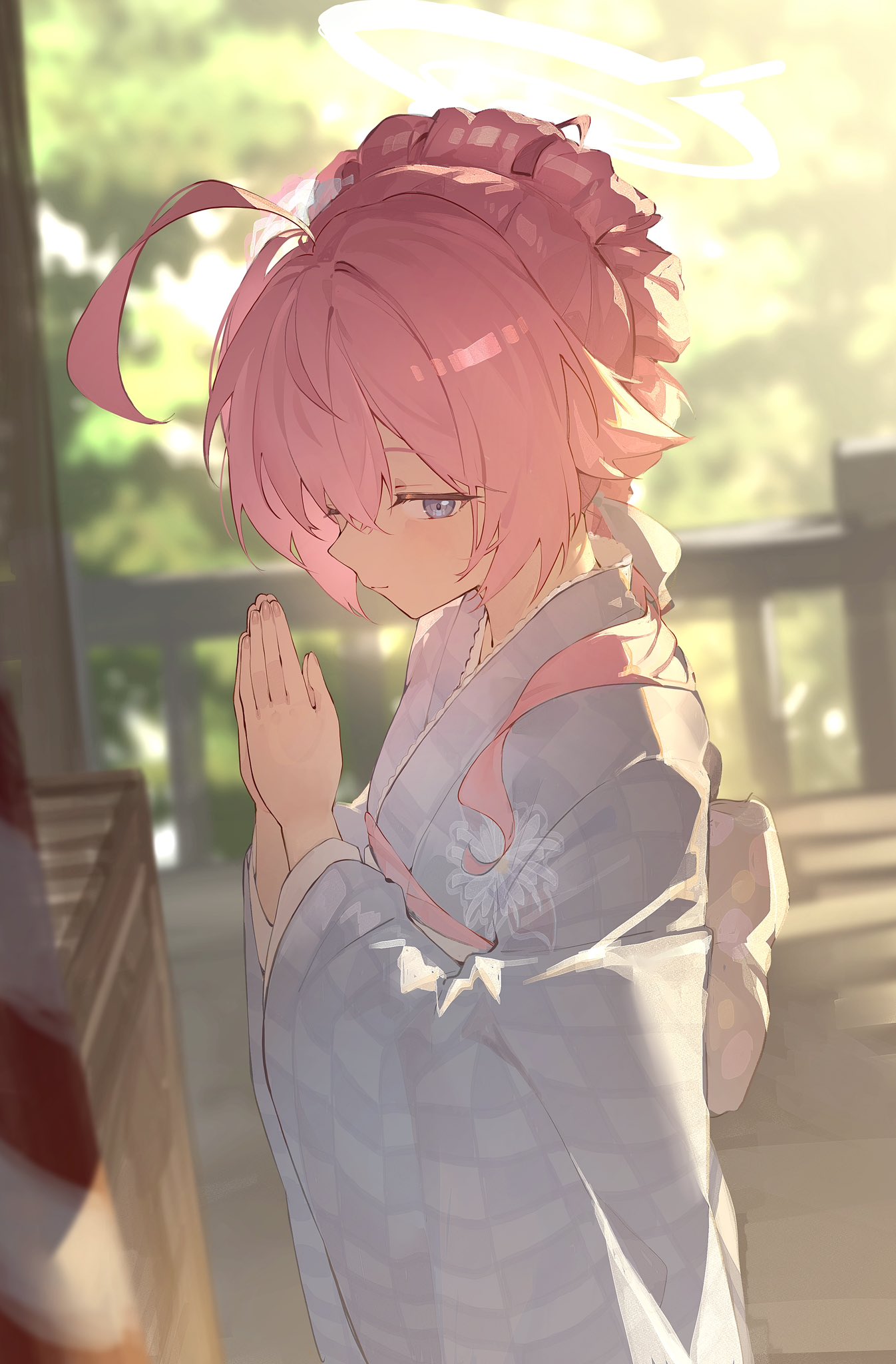 the image shows a beautiful anime girl with pink hair styled in a bun, wearing a light blue and white patterned kimono. she is standing outdoors in a sunlit setting, possibly near a temple or shrine, with her hands clasped together in a prayerlike gesture. a faint halo appears above her head, adding to the serene and peaceful atmosphere. the art style is soft and dreamy, with a focus on light and color. the overall impression is one of tranquility and spiritual devotion.