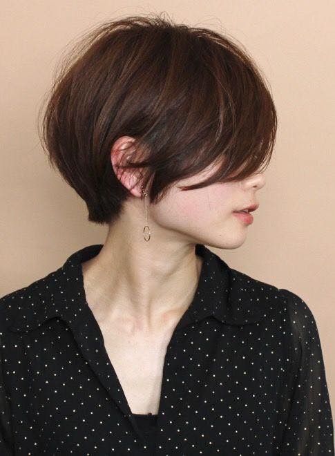 a young woman with short, dark brown hair is wearing a black polka dot blouse. she is looking off to the side, with her head tilted slightly. she is wearing gold earrings.  she is in a casual, simple pose. the photo is taken in a studio setting.