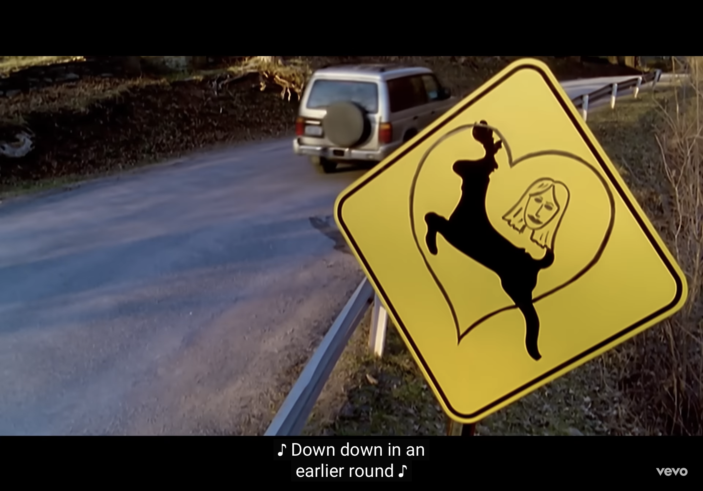 a yellow deer crossing sign is displayed prominently in the foreground on the right side of the image. however, instead of the typical deer silhouette, this sign features a stylized deer with a woman's face superimposed on its rear end.  a silver suv is driving away from the sign in the background, heading down a paved road that curves gently to the left. the surrounding environment is wooded and appears to be rural. the lighting suggests a sunny day, with shadows cast by the trees and the sign. the overall impression is one of humor and lightheartedness, with a touch of the surreal.