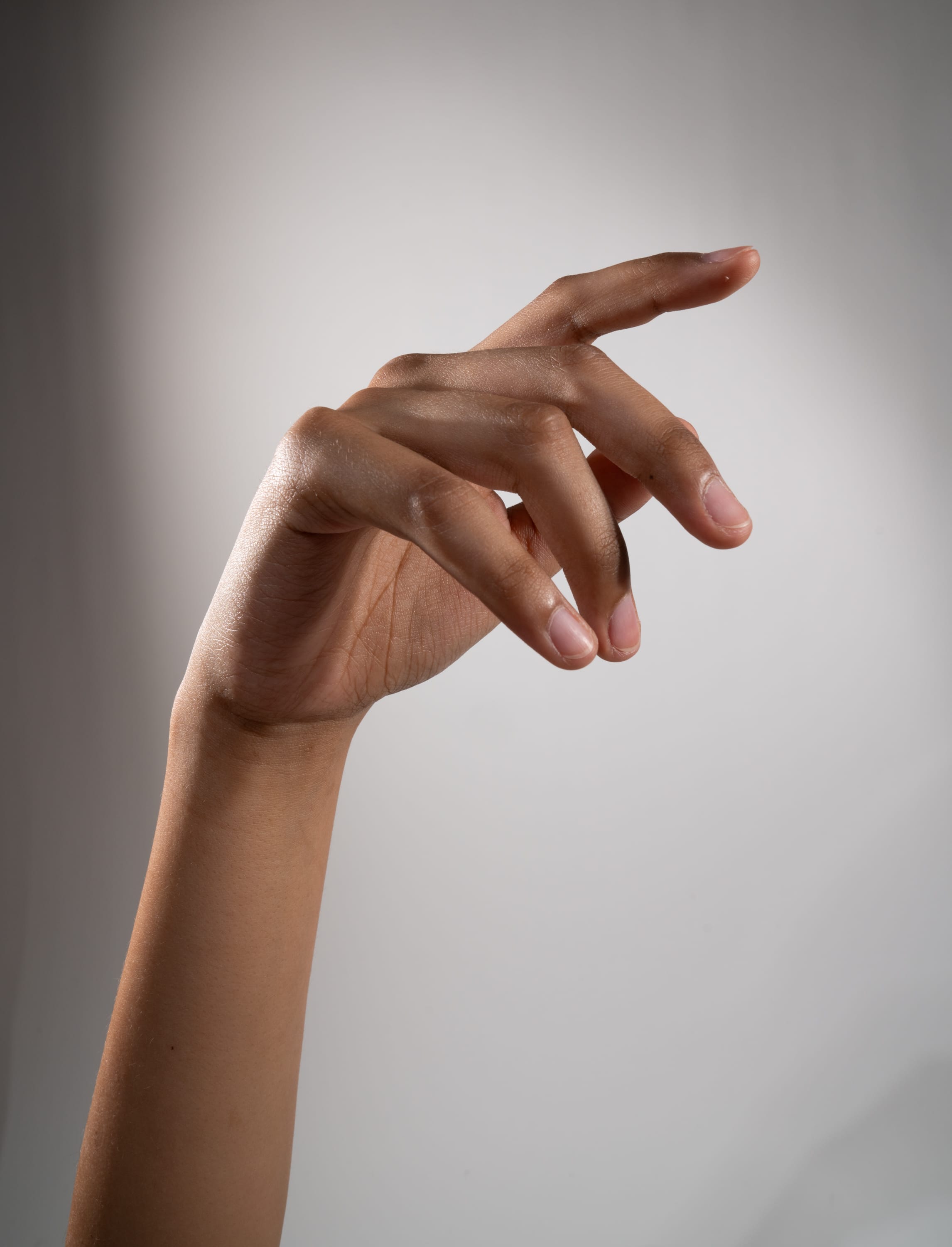the image shows a hand with its fingers slightly curled in, reaching towards the right side of the frame. the hand is positioned against a plain gray background, illuminated by studio lighting. the closeup perspective emphasizes the details of the hand's shape and skin tone.