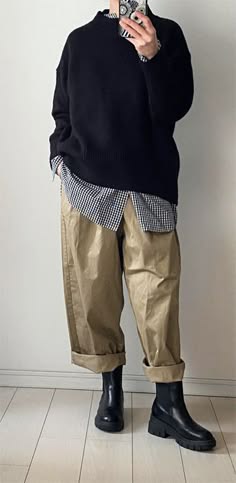 a person wearing a black sweater, beige trousers and black boots is standing on a light tiled floor.