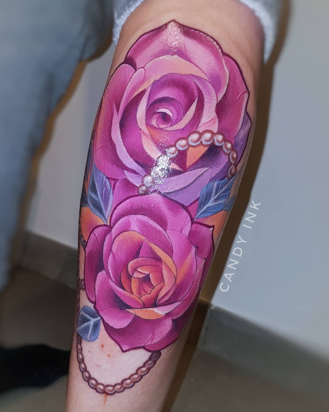 a person's arm with a tattoo of two pink roses with draped pearls.