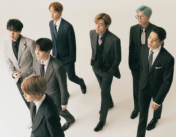 seven men in stylish suits pose against a white background. they stand in various positions, some looking at the camera and others looking away. the image exudes a sophisticated and fashionable aura, highlighting their individual styles and the group's cohesive image.