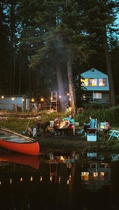an image of a group of friends enjoying a campfire by a lake at night.  they are sitting around a small fire, playing music, and relaxing. a canoe is resting on the lake's edge, and a cabin can be seen in the background, nestled within a dark forest. string lights are visible, adding to the cozy and tranquil atmosphere. the scene exudes a sense of peacefulness and the beauty of nature.
