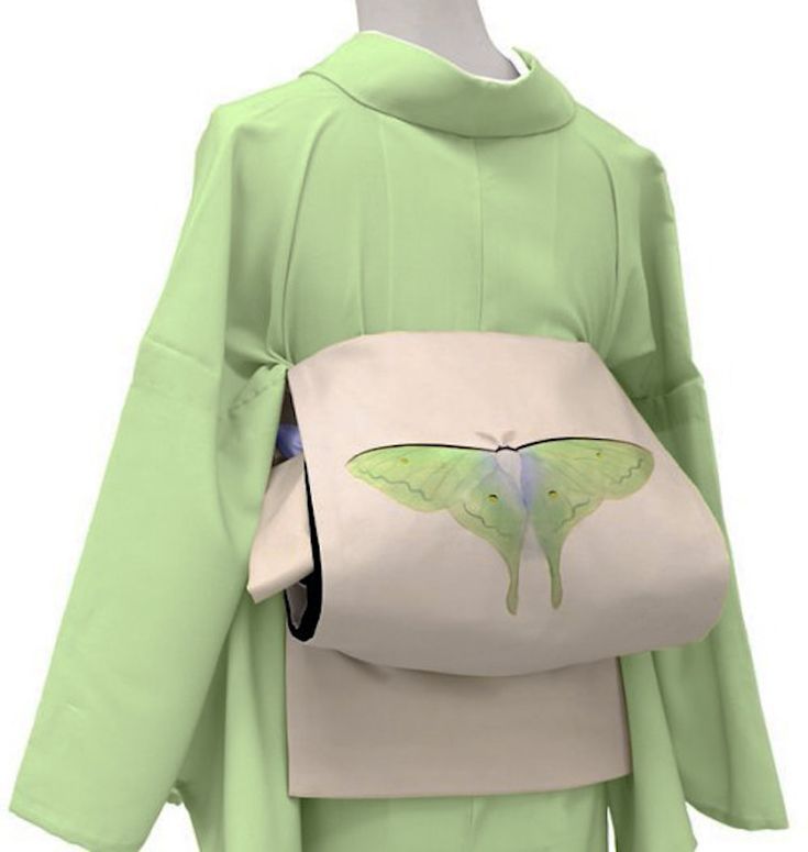an image of a light green kimono with a moth design on the obi. the kimono is styled in a traditional japanese manner, with the obi cinching the waist and adorned with a drawing of a luna moth. the garment is displayed on a mannequin.