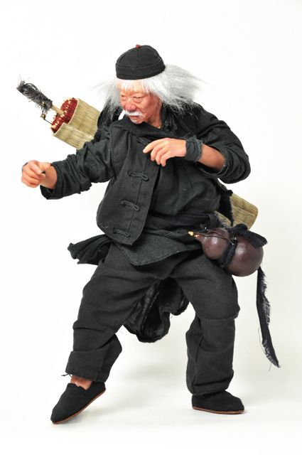 a senior asian man in a black outfit and black hat is doing martial arts moves. he has long white hair and is holding a weapon. he looks angry and ready to fight.