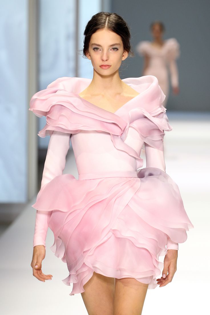 a model walks the runway wearing a stunning pink gown, showcasing the latest haute couture fashion. the dress is adorned with delicate ruffles and has a feminine, elegant silhouette. the model's graceful pose and the intricate details of the dress create a captivating image of elegance and sophistication.