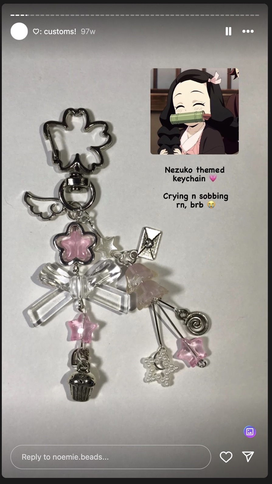 a screenshot of an instagram story showing a custom nezukothemed keychain. the keychain is decorated with pink stars, hearts, bows, and a cupcake charm. next to the keychain is a picture of the anime character nezuko. the text on the screen reads "nezuko themed keychain" and "crying n sobbing rn, brb." the story is from "@customs!" and was posted 97 weeks ago. there is a reply bar at the bottom that says "reply to noemie.beads..."