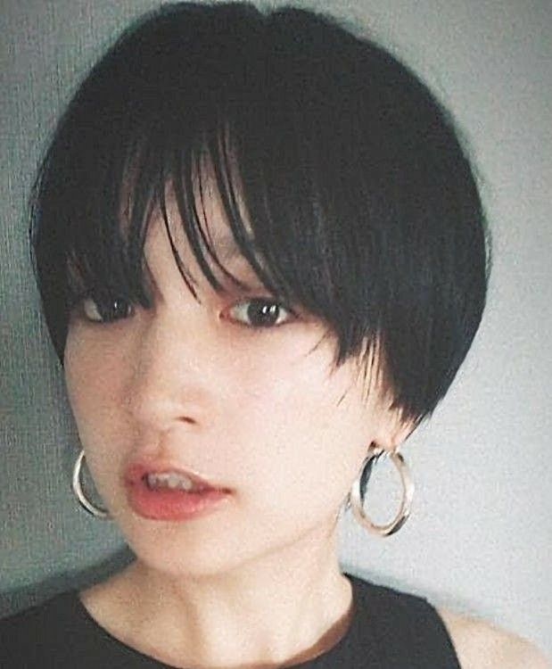 a woman with short black hair that is styled in a blunt bob with bangs. she is wearing silver hoop earrings and has light makeup on. she is looking directly at the camera with a serious expression on her face.