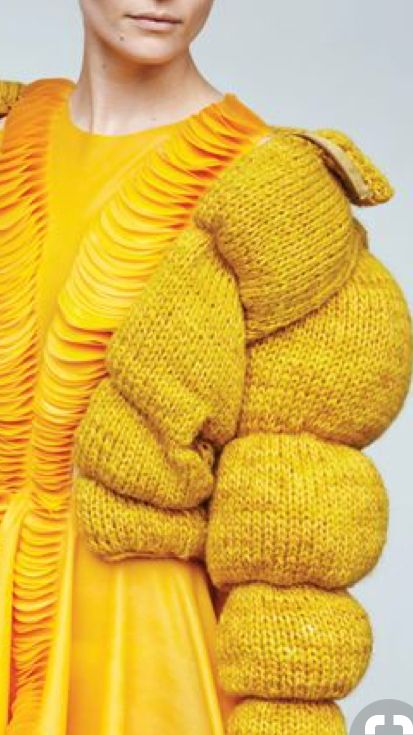 a closeup of a woman wearing a vibrant yellow knitted sweater, showcasing a unique design with puffed sleeves. the sweater is crafted with a textured knit, highlighting the intricate details and adding a touch of luxury. the model's elegant pose and the vibrant yellow color scheme create a captivating visual, emphasizing the beauty and uniqueness of the garment.