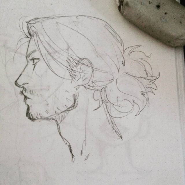 a pencil sketch of a man's side profile. the man has long hair that is pulled back into a loose messy bun. the sketch is simple and unfinished but clearly shows the man's features. the lines are light and the paper is visible. the drawing is in a sketchbook, which is visible in the background. the image is cropped to focus on the man's face and hair.
