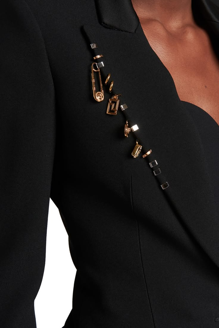 a closeup of a black blazer adorned with gold jewelry resembling safety pins and geometric shapes.