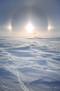 a panoramic view of a vast, snowy landscape with three sun dogs, or mock suns, in the sky. the sun is shining brightly, creating a halo around itself and the two sun dogs. the snow is pristine white, and the horizon is distant.  the wind has sculpted the snow into intricate patterns, creating a mesmerizing landscape that is both beautiful and otherworldly.