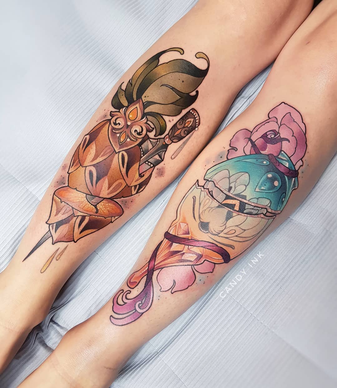 a pair of legs with two colorful tattoos on them.  the tattoo on the left leg is of a dagger stabbing a crystal.  there are green and brown accents on the dagger's handle.  the tattoo on the right leg is of a broken crystal with a pink and purple flower.  the image is a closeup shot of the tattoos.