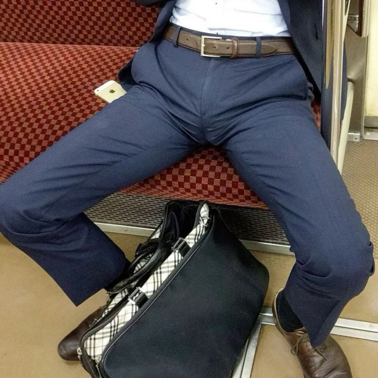 a man in a blue suit is sitting in a subway car with a bag on his lap and a phone in his pocket. he is wearing brown leather shoes. the subway car is covered in a checkered pattern. he is also wearing a white shirt. he is dressed in a casual business style.  the image is taken from a perspective looking down at the man.
