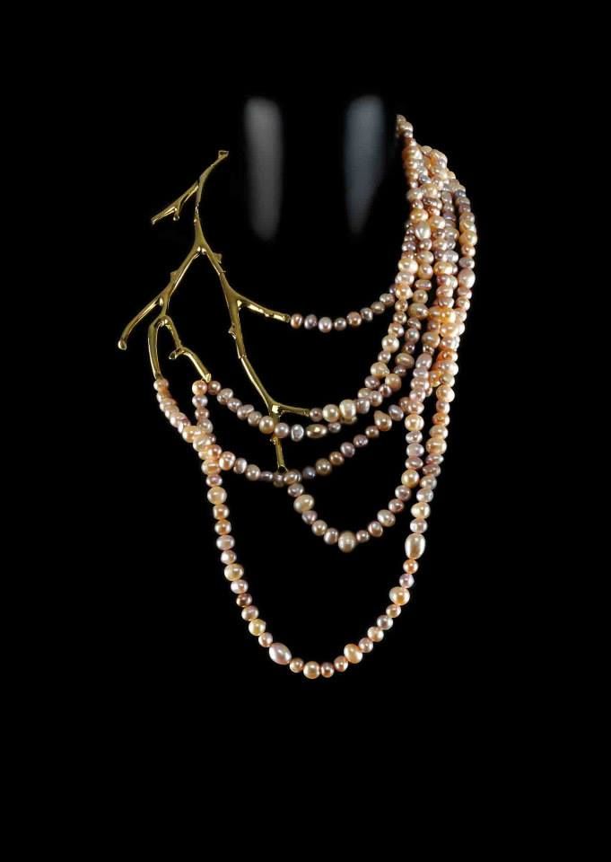 a multilayered pearl necklace with a gold branch design sits on a black background. the necklace is made up of several strands of pearls, which are arranged in a cascading pattern. the gold branch adds a touch of elegance and sophistication to the necklace. the overall effect is one of delicate beauty and timeless elegance.