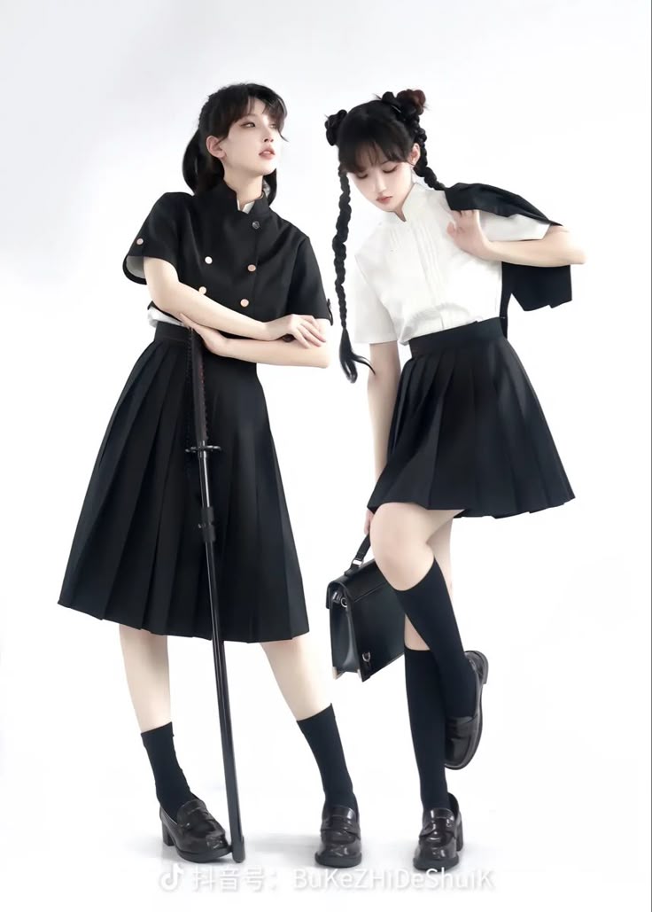 two young asian women are standing in a studio setting against a white background, posing in similar black and white uniforms. the woman on the left wears a black, shortsleeved buttondown shirt with gold buttons and a black pleated skirt, black kneehigh socks, and black loafers. she is holding a sword, resting it on the ground. the woman on the right wears a white, shortsleeved buttondown shirt, a black pleated skirt, black kneehigh socks, and black loafers. she has a black blazer draped over her shoulder and holds a black shoulder bag. both women have dark hair styled in pigtails or buns. the style of clothing seems to be modern hanfu.