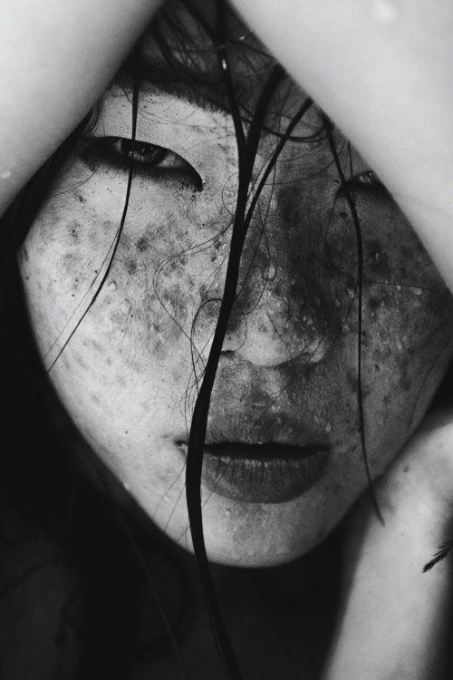 a closeup, black and white portrait of a woman's face. her face has freckles and wet hair strands, and the image focuses on the texture of her skin. the framing is tight, emphasizing her features.