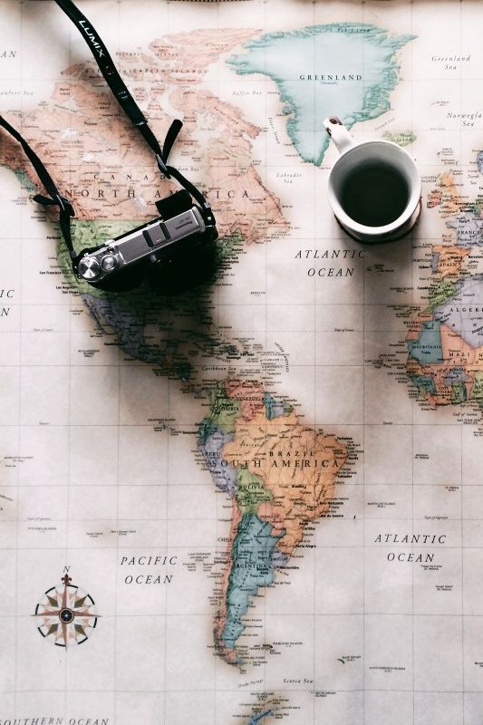 a topdown shot features a world map, a camera with a "lumix" strap, and a cup of coffee. the map showcases the continents and oceans in a vintage style. the camera is positioned on the left side of the map, while the coffee cup rests near greenland.