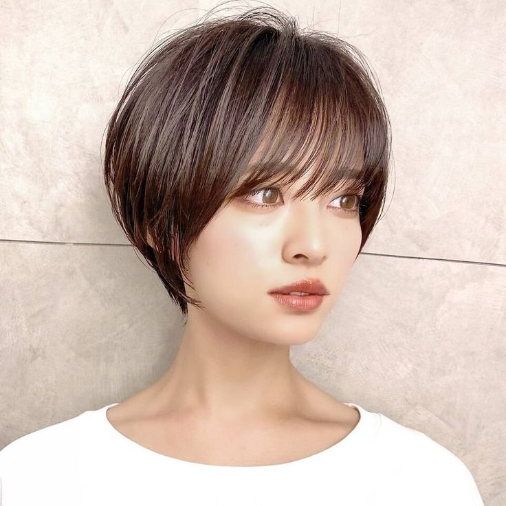 closeup portrait of a young japanese woman with short brown bob hairstyle with bangs, looking to the right side. she is wearing white shirt and has flawless makeup.  she has a soft, happy expression on her face. the background is white.