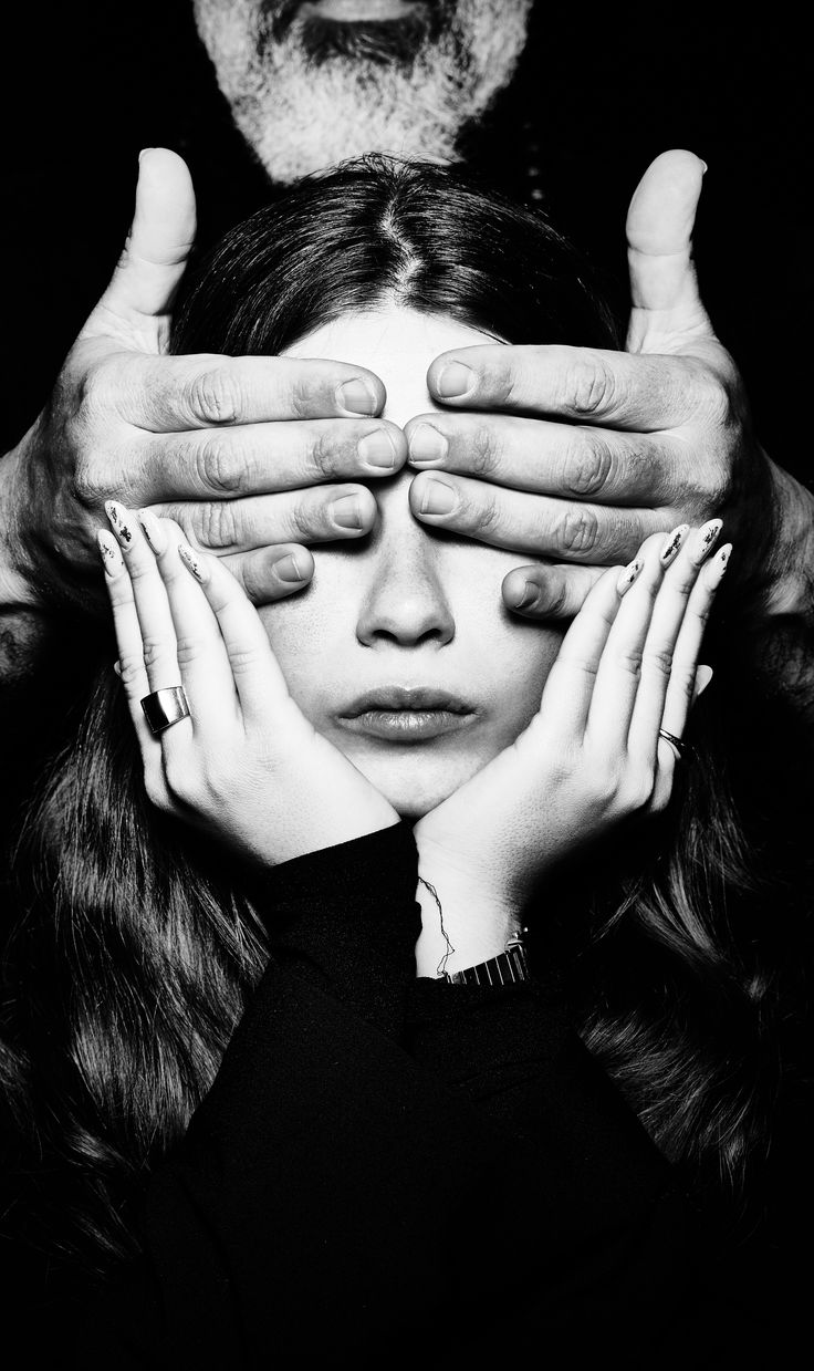 a woman's face is partially obscured by the hands of a man, black and white photo.