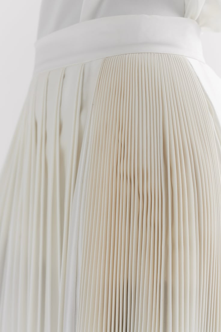 closeup shot of a pleated white skirt or dress. the image emphasizes the texture and design of the fabric, with the pleats creating a repeating vertical pattern. the folds and shadows add depth to the garment, highlighting the craftsmanship and details of the clothing.