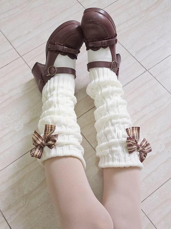 the image showcases a pair of women's legs adorned with stylish elements of lolita fashion. the focal point is a pair of white, cableknit leg warmers that extend from the feet to just below the knees. each leg warmer is accented with a charming brown and creamcolored bow near the top. the model wears brown leather platform shoes featuring a mary jane style with a single strap across the foot, adding a touch of vintage flair. the shoes and socks complement each other beautifully, creating a cohesive and eyecatching look. the photo is taken from a high angle, allowing for a clear view of the details and textures of the garments. the background features lightcolored tiles, providing a neutral backdrop that doesn't distract from the main subject.  the overall aesthetic is sweet, feminine, and slightly nostalgic, reflecting the essence of lolita fashion.