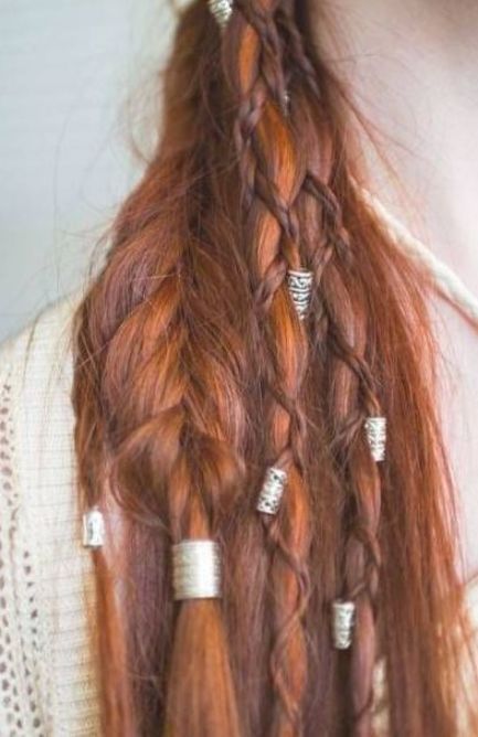 this image shows a hairstyle featuring several braids and silver colored beads. the hair is auburn and long. the braids are styled in different ways, including a standard braid, a crown braid, and smaller braids wrapped around the main hair. the hair beads add a decorative touch to the hairstyle. the style is reminiscent of viking or fantasyinspired hairstyles.