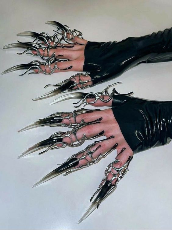 a pair of hands modeling long, clawlike nails adorned with silver wire accents. the nails are a translucent gray, while the model wears sleek black gloves. the image appears to be showcasing unique and edgy fashion accessories.